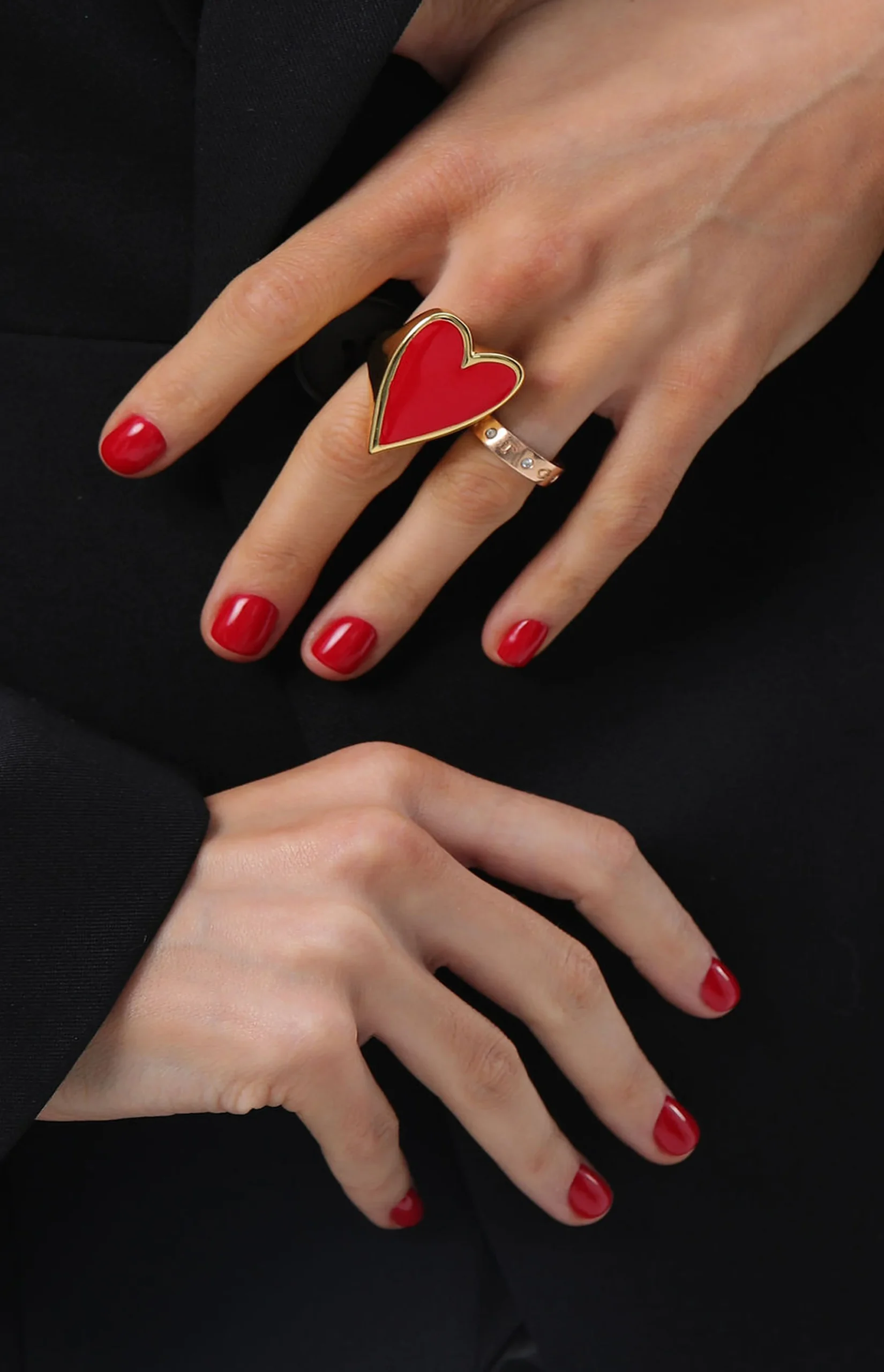 Dwie dłonie z czerwonym manicure i pierścionkami-sercami.