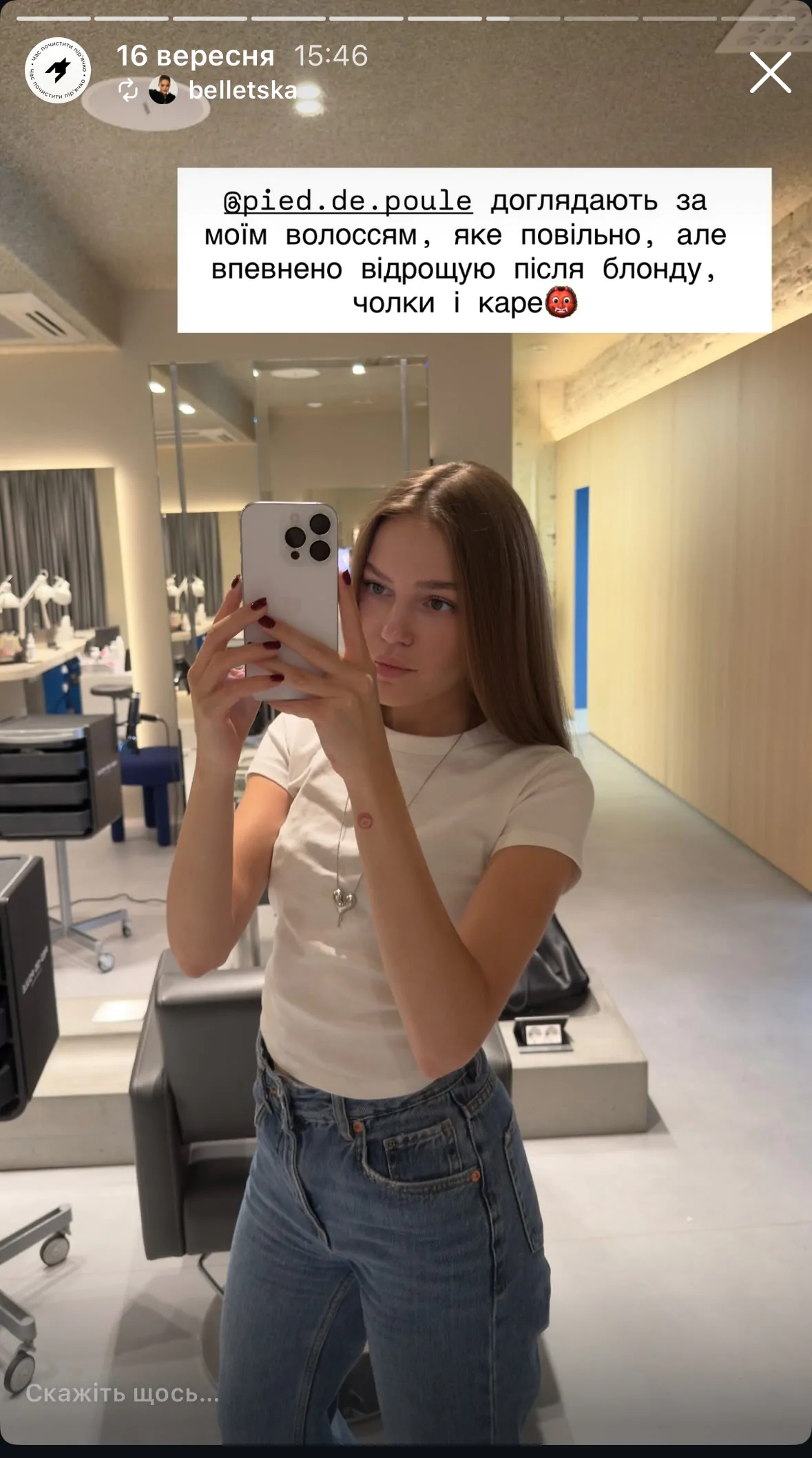 Kobieta w t-shircie i jeansach robi selfie w salonie.