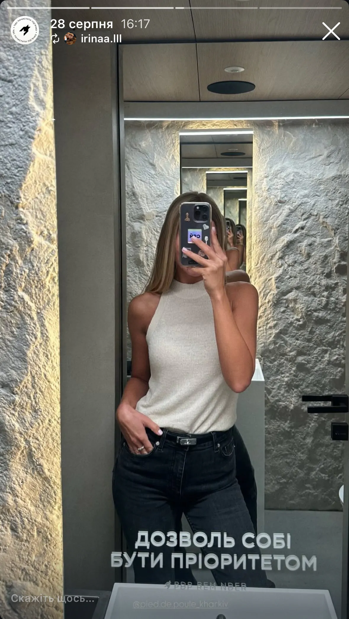 Kobieta w topie i jeansach robi selfie w lustrze.