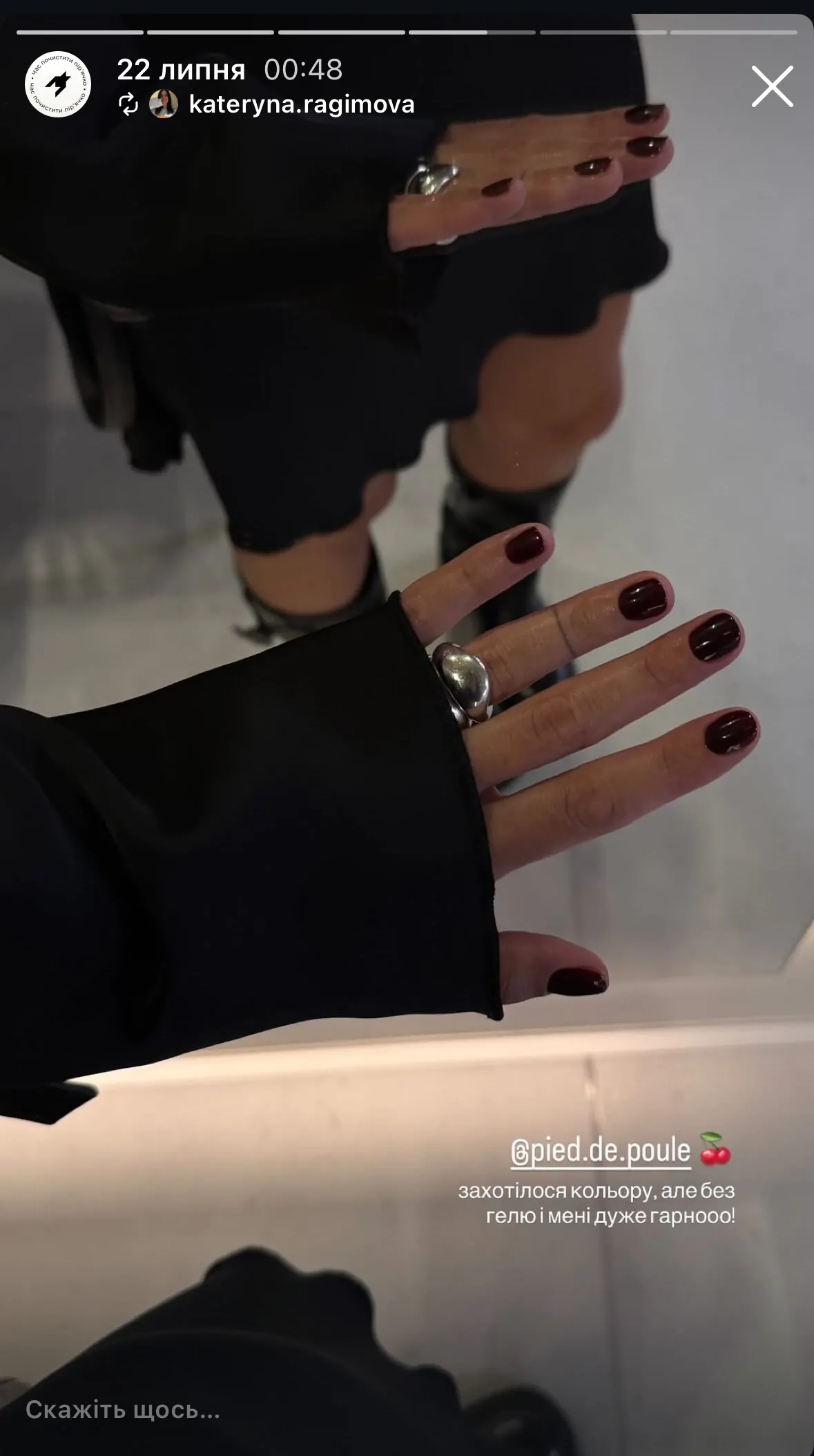 Lustrzane odbicie dłoni z eleganckim, bordowym manicure i dużym srebrnym pierścionkiem na tle czarnej stylizacji.